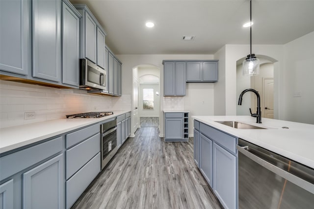 kitchen featuring a sink, gray cabinets, arched walkways, light wood finished floors, and stainless steel appliances