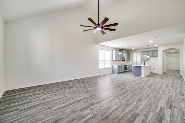 unfurnished living room with a ceiling fan, wood finished floors, high vaulted ceiling, arched walkways, and a sink