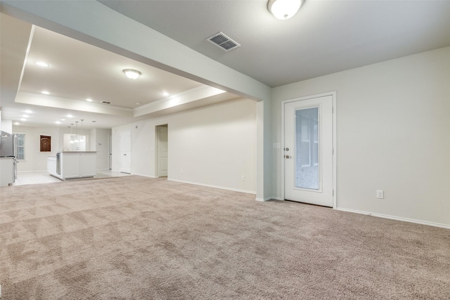 interior space with a tray ceiling, visible vents, light carpet, and baseboards