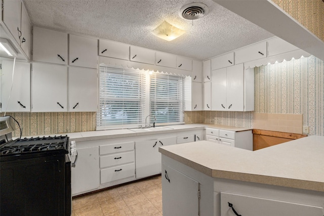 kitchen with visible vents, gas range, a sink, light countertops, and wallpapered walls