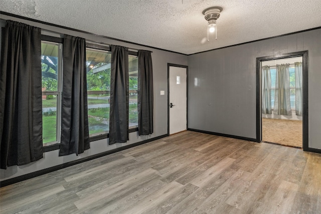 spare room featuring crown molding, a textured ceiling, baseboards, and light wood finished floors