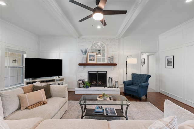 living room featuring crown molding, a decorative wall, wood finished floors, a fireplace, and ceiling fan