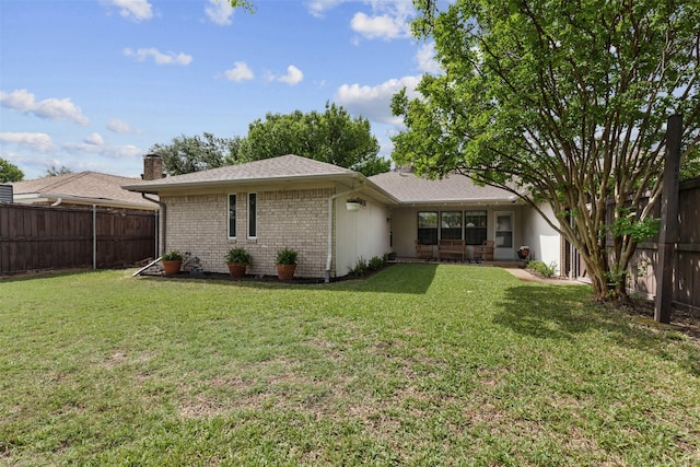 back of house featuring a fenced backyard, a chimney, a yard, and brick siding