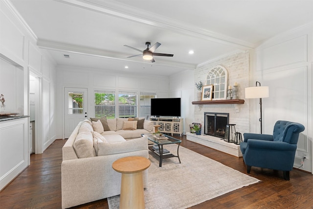 living room with ceiling fan, a fireplace, a decorative wall, dark wood-type flooring, and ornamental molding