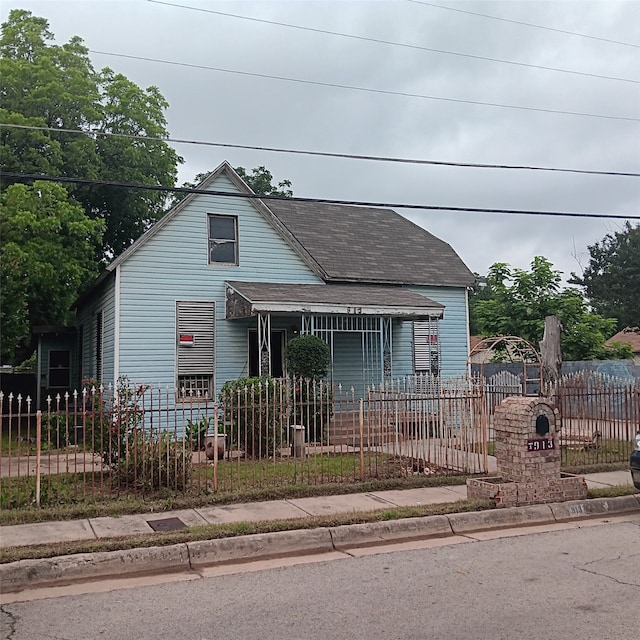 view of front facade with a fenced front yard, roof with shingles, and covered porch