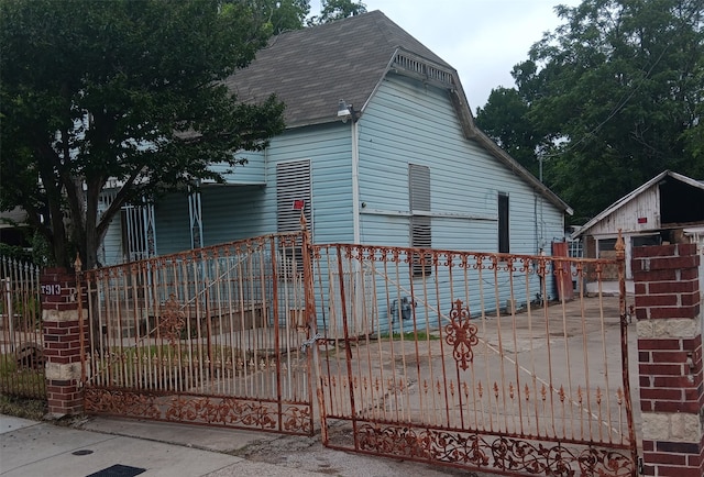 view of side of property with fence private yard, a shingled roof, a gate, and an outdoor structure