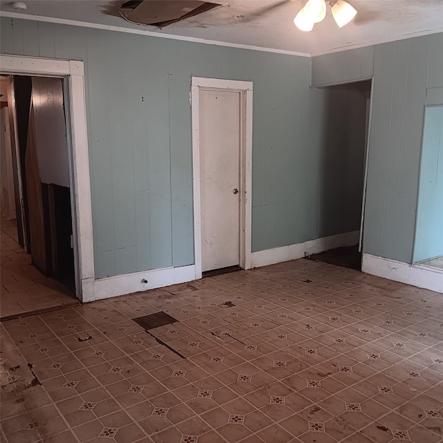 unfurnished room featuring wooden walls, baseboards, and ornamental molding