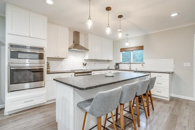 kitchen with a breakfast bar area, dark countertops, appliances with stainless steel finishes, tasteful backsplash, and wall chimney exhaust hood