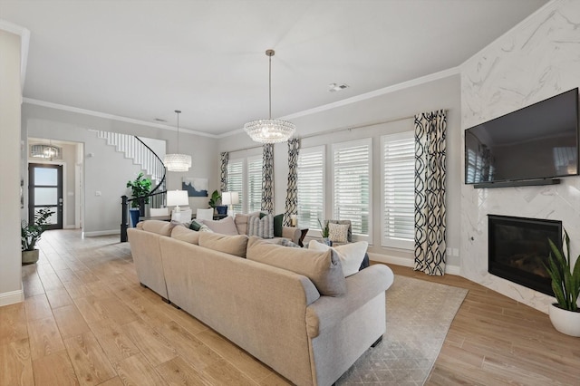 living area featuring ornamental molding, a fireplace, light wood-style floors, baseboards, and stairway
