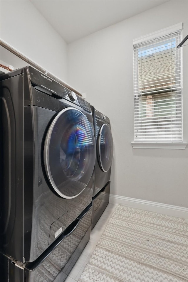 clothes washing area featuring laundry area, baseboards, tile patterned flooring, and washing machine and clothes dryer