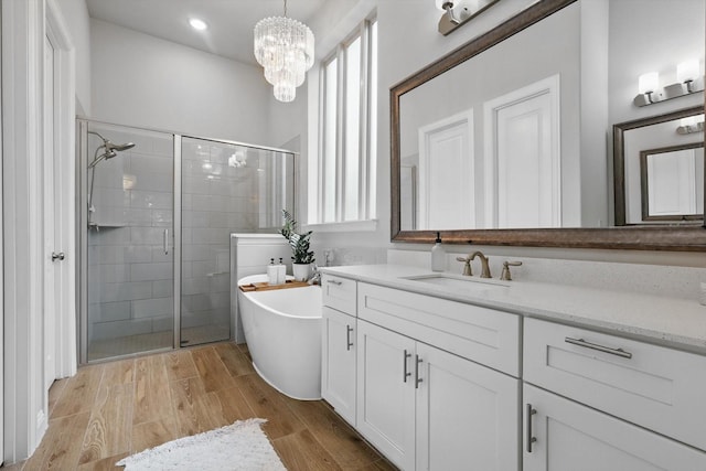 full bathroom with vanity, an inviting chandelier, a freestanding tub, wood finished floors, and a shower stall