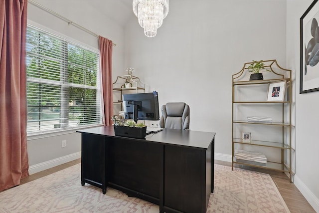 office space featuring baseboards, light wood finished floors, a healthy amount of sunlight, and an inviting chandelier