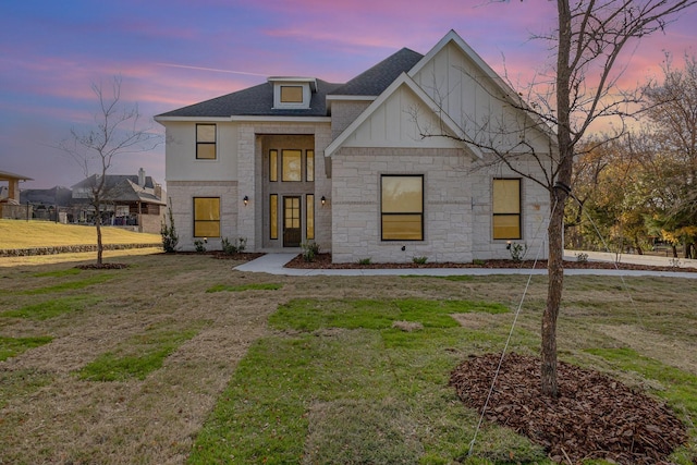 modern farmhouse featuring a yard, roof with shingles, board and batten siding, and stone siding