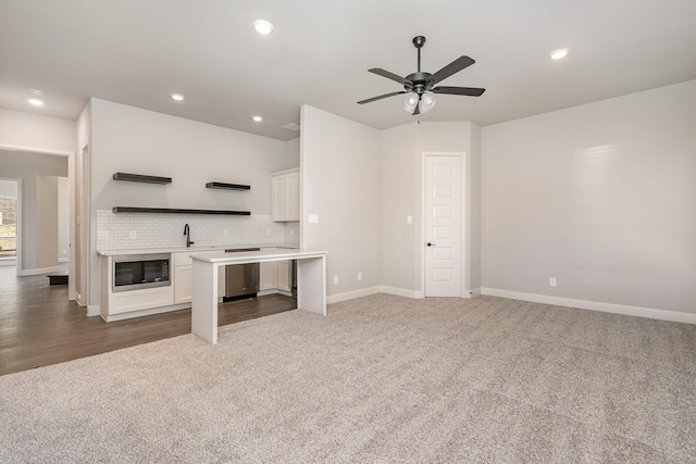 unfurnished living room with a sink, carpet floors, baseboards, and a ceiling fan
