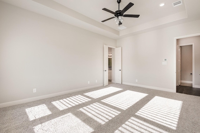 carpeted spare room with visible vents, a raised ceiling, ceiling fan, and baseboards