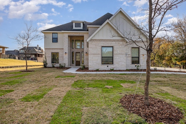 view of front of house featuring roof with shingles, a front yard, and stone siding