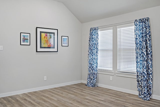 empty room with light wood-style floors, baseboards, and lofted ceiling