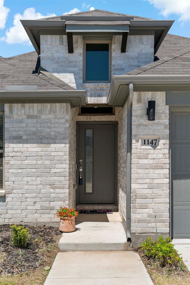 entrance to property with a shingled roof and an attached garage