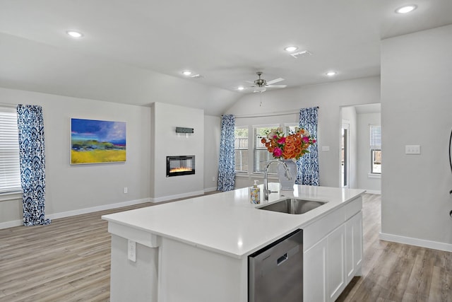 kitchen with dishwasher, a sink, baseboards, light wood finished floors, and a glass covered fireplace