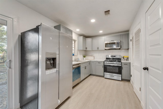 kitchen with light wood-style floors, light countertops, gray cabinets, a sink, and appliances with stainless steel finishes