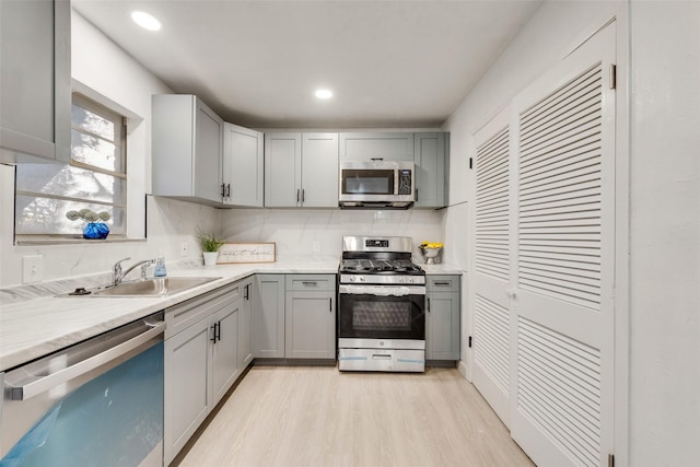 kitchen featuring a sink, light countertops, gray cabinets, light wood-style flooring, and stainless steel appliances