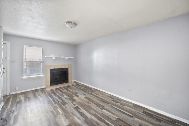 unfurnished living room featuring baseboards, a textured ceiling, wood finished floors, and a tile fireplace