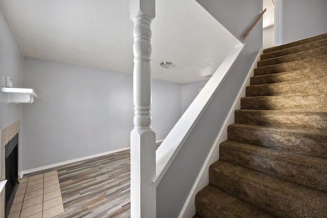 stairs featuring a tiled fireplace, baseboards, and wood finished floors
