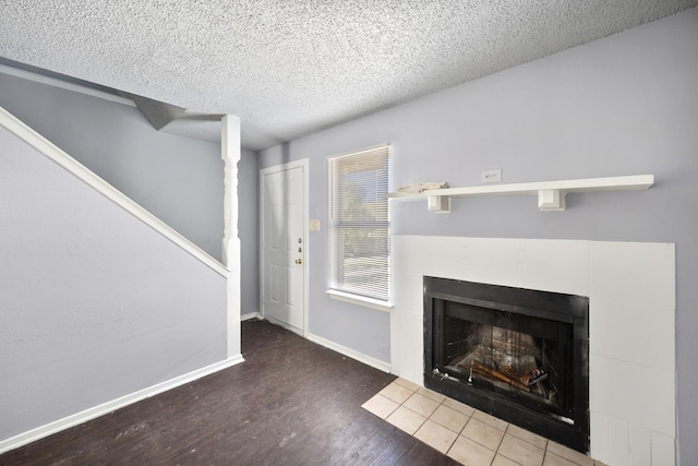 unfurnished living room with a textured ceiling, wood finished floors, a tile fireplace, stairway, and baseboards
