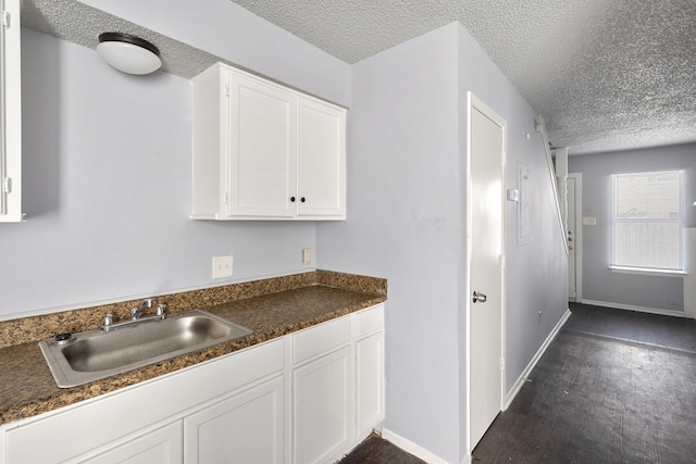 kitchen featuring a sink, a textured ceiling, white cabinets, and dark countertops