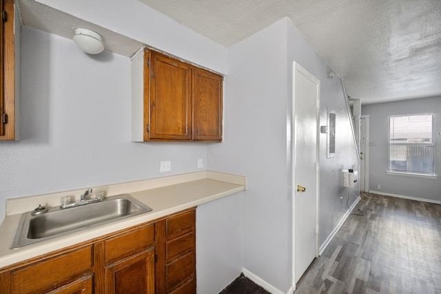 kitchen with brown cabinetry, dark wood-style flooring, a textured ceiling, a sink, and light countertops