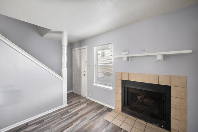 unfurnished living room with a tiled fireplace, baseboards, and wood finished floors