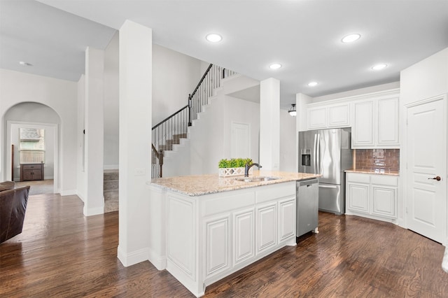 kitchen with white cabinets, light stone counters, a sink, stainless steel appliances, and dark wood-style floors
