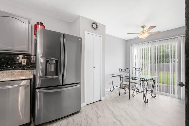 kitchen with decorative backsplash, light stone countertops, baseboards, a ceiling fan, and stainless steel appliances