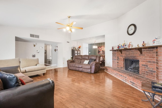 living room with a fireplace, ceiling fan with notable chandelier, wood finished floors, and visible vents
