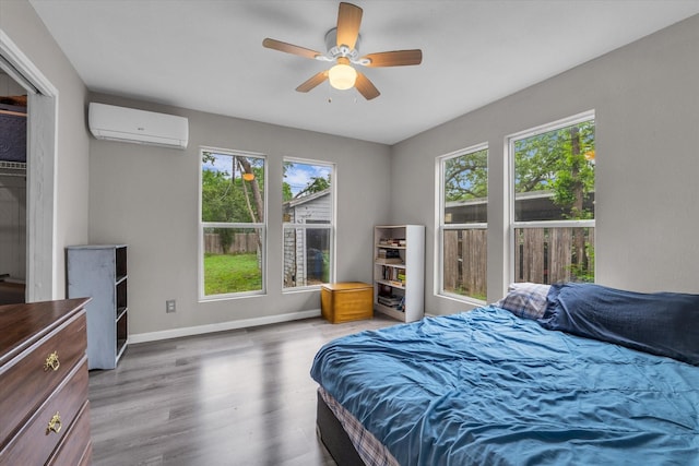 bedroom featuring ceiling fan, baseboards, a wall mounted AC, and wood finished floors