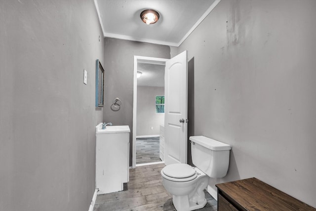 half bathroom with crown molding, wood finished floors, toilet, baseboards, and a sink