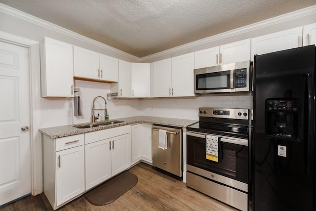 kitchen with light stone countertops, a sink, stainless steel appliances, white cabinetry, and wood finished floors