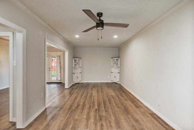 empty room with a ceiling fan, a textured ceiling, crown molding, wood finished floors, and baseboards