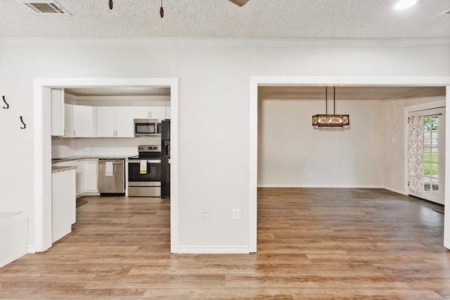 unfurnished dining area featuring a textured ceiling, visible vents, ornamental molding, and light wood-type flooring