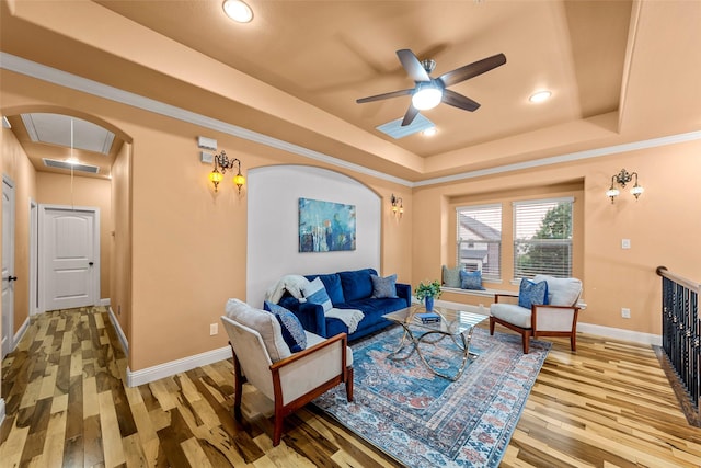 living area with visible vents, light wood-style floors, ceiling fan, a raised ceiling, and arched walkways