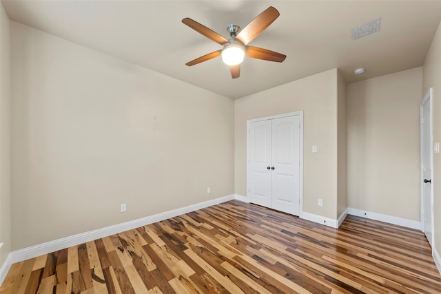 unfurnished bedroom featuring a ceiling fan, visible vents, wood finished floors, baseboards, and a closet