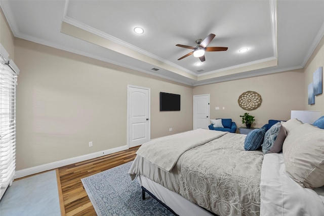 bedroom with visible vents, wood finished floors, a raised ceiling, baseboards, and ornamental molding