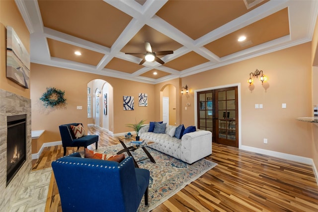 living room featuring arched walkways, baseboards, a lit fireplace, and light wood-type flooring