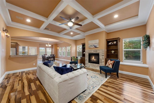 living room with light wood finished floors, arched walkways, a stone fireplace, baseboards, and visible vents