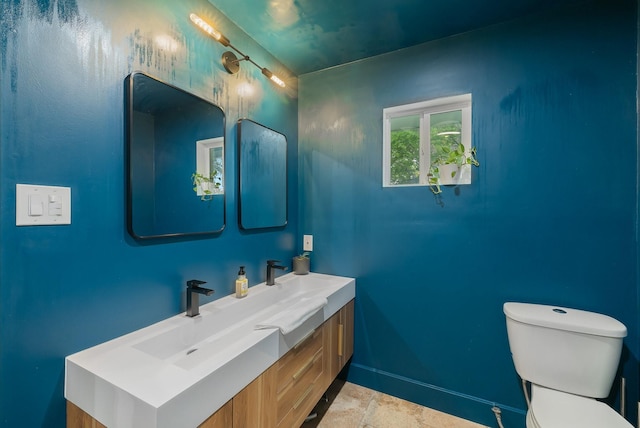 bathroom featuring toilet, baseboards, stone finish flooring, and vanity