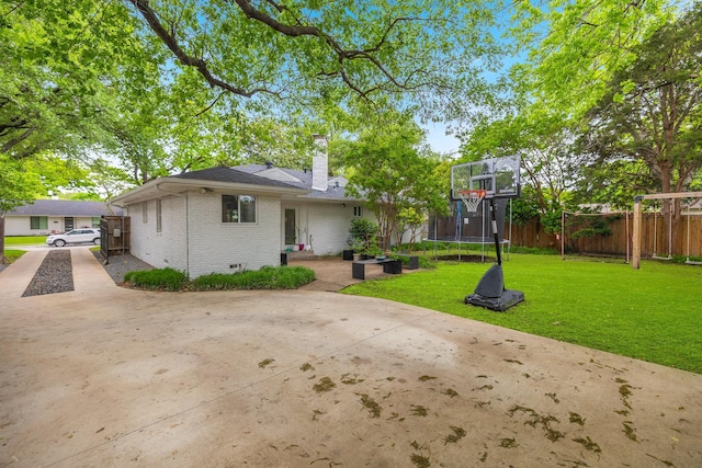 rear view of property with fence, a chimney, brick siding, a trampoline, and a yard