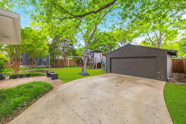 view of patio with a trampoline, a detached garage, fence, an outdoor structure, and a playground