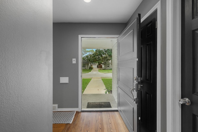doorway with baseboards, a textured wall, and wood finished floors