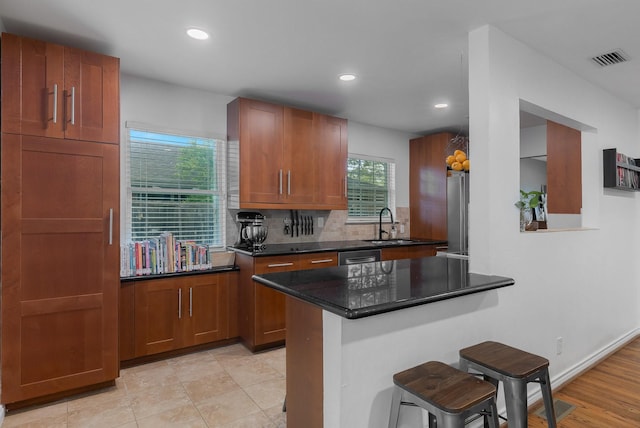 kitchen with brown cabinets, a breakfast bar, a sink, recessed lighting, and decorative backsplash