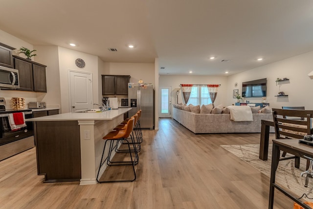 kitchen featuring dark brown cabinets, a sink, light wood-style floors, light countertops, and stainless steel appliances